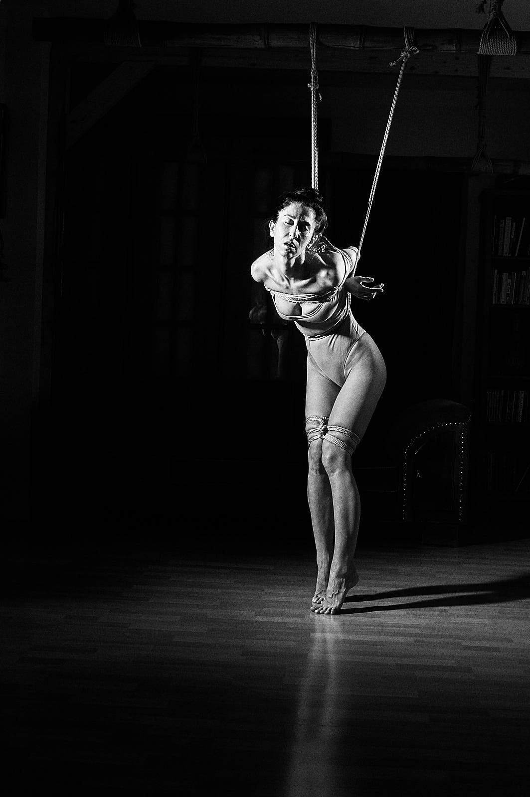 This picture depicts kinbaku photpgraphy in black and white film style. A beautiful woman with long black hair in rope bondage.
