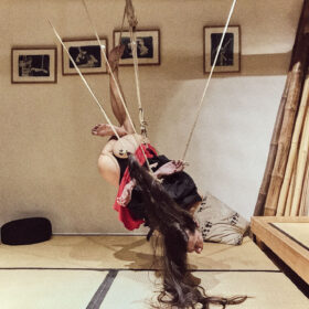 Natasha Nawataneko in semanawa kinbaku suspension, red skirt, black hair