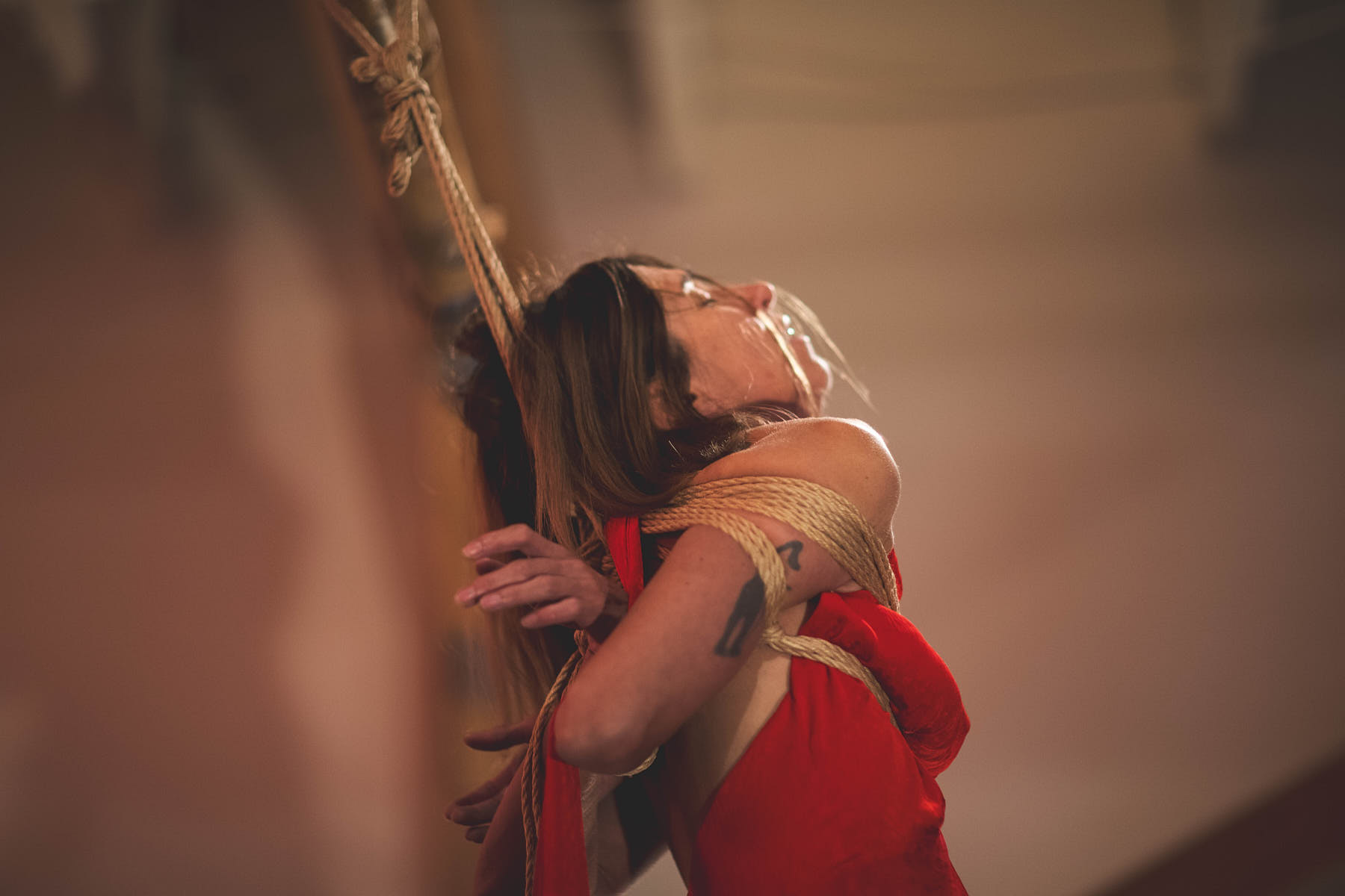 Nawataneko kinbaku model and performer being tied in Gote hands on the back in the red dress presenting in San Francisco